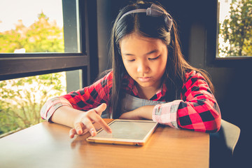 Girl is using tablet while sitting in library and reading a book