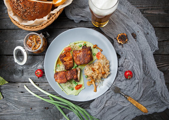 rustic composition: pork on grill on pea puree with stewed cabbage and mushrooms with a glass of beer on a wooden table