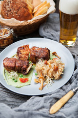 rustic composition: pork on grill on pea puree with stewed cabbage and mushrooms with a glass of beer on a wooden table