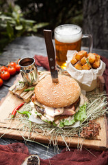 rustic composition: a large juicy burger with baked potatoes and beer on a wooden background