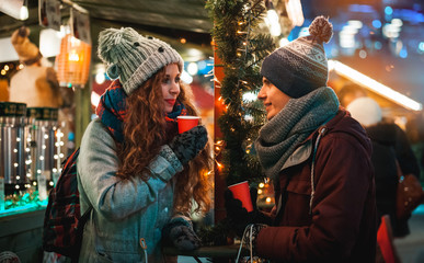 Fototapeta na wymiar Christmas market restaurant at evening, couple with hot drinks in fairy surroundings