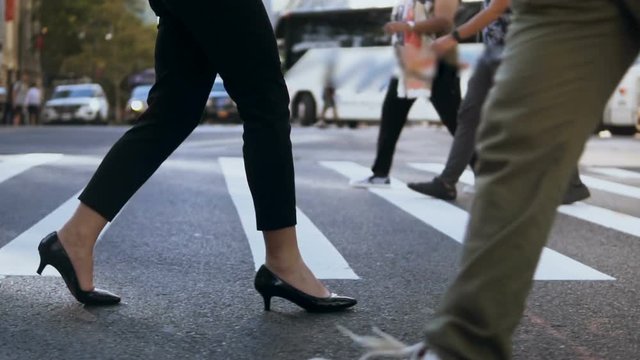 Close-up view of young businesswoman wearing shoes with heels crossing the road in busy downtown. Slow motion.