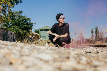 Naklejka na ściany i meble .Young modern tattoed woman dressed in black at an abandoned train station, playing with colorful smoke between train tracks. Lifestyle portrait