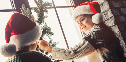Decorating home for Christmas. Couple kids Little girl and boy  in santa klaus hat make decor for...