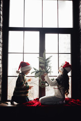 Decorating home for Christmas. Couple kids Little girl and boy  in santa klaus hat make decor for window. Holidays  family tradition. Happy New Year!