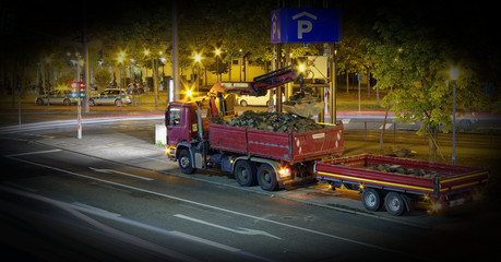 LKW mit Kran bei nächtlichen Bauarbeiten und Abladen von Steinen in der Stadt