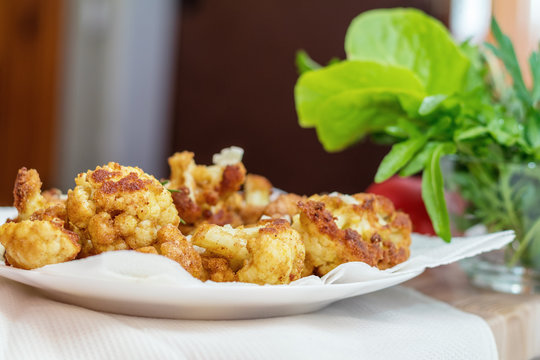 Fried cauliflower in batter on a white plate with white napkin. Close-up