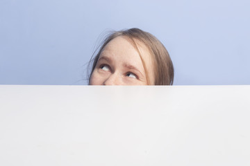 Girl looks up. Top of female face behind white banner, isolated on blue background