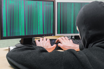 The hacker in a mask hacks the computer system. Zeros and ones are shown on the screen.