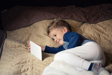 Happy kid watching cartoons on touchpad while resting on the bed.