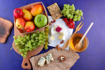 Camembert, cheese with mold, apples, green grapes, honey, red berries of viburnum, peanuts, dark blue background, pop art, retro style, pears, healthy food, cheddar on parchment paper, art