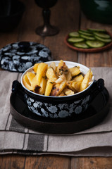 On a wooden table a dish of fried potatoes, in the background a plate with fresh cucumbers, sliced ​​slices