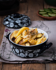 On a wooden table a dish of fried potatoes, in the background a plate with fresh cucumbers, sliced ​​slices