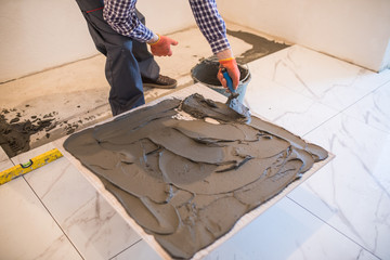 man hand troweling adhesive for ceramic tile flooring. Laying Ceramic Tiles.