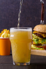 Beer with burger and fries on dark wooden background. Ale and food, vertical