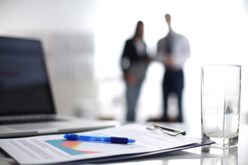 Laptop computer with folder on desk , two businesspeople standing in the background