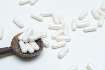 White tablets on a medicine dose spoon, with tablets across the table