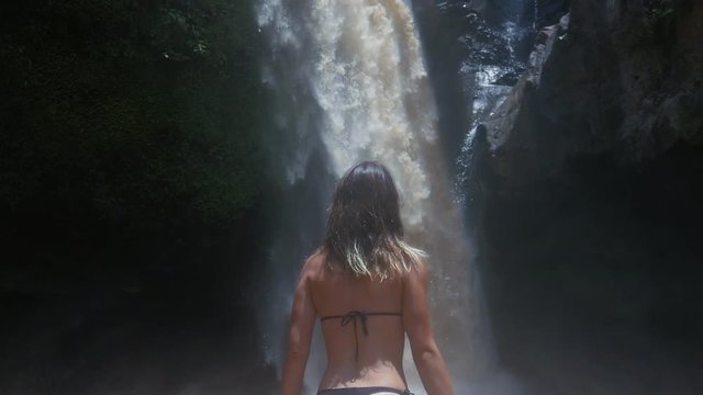 young beautiful woman in bikini posing near waterfall in jungle at bali