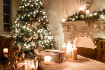 the gifts on the table. Christmas evening by candlelight. classic apartments with a white fireplace, decorated tree, sofa, large windows and chandelier.