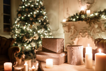 the gifts on the table. Christmas evening by candlelight. classic apartments with a white fireplace, decorated tree, sofa, large windows and chandelier.