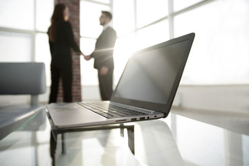 laptop on the desk, background handshake