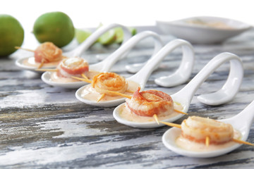Fototapeta na wymiar Ceramic spoons with bacon wrapped scallops and sauce on wooden table