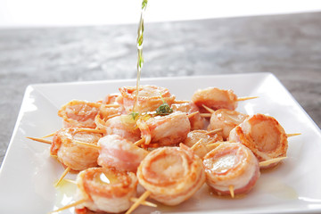 Adding oil to bacon wrapped scallops on plate