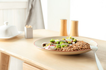 Plate with buckwheat porridge and vegetables on table