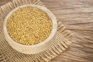 Alfalfa seeds in white ceramic bowl on wooden background from above