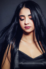 Fototapeta premium Beautiful brunette girl with black long hair on a dark background close-up