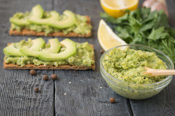 The knife with the bowl with pate avocado and crunchy toast on a dark rustic wooden table.