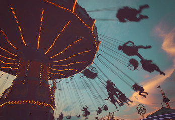  local fair at dusk with people riding swinging rides and enjoying the summer atmosphere toned with...