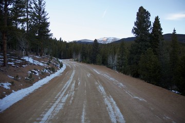 Fototapeta na wymiar Snow covered dirt road winding through pines up a mountain