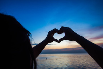 Silhouette of hand sign heart on twilight sky after sunset.