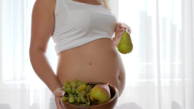 hand female close-up holds dish with fructis near big naked tummy beside window at room