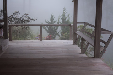 wood balcony in mist & fog. terrace in cold autumn evening. chair in mysterious forest.