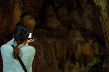 woman take photo of stone cave. tourist take picture of cavern with stalactite.