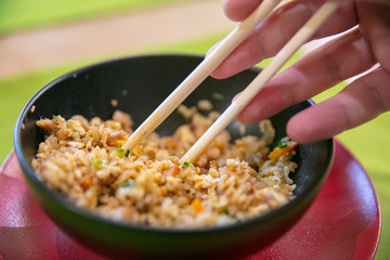 Rice with vegetable in  black plate and chopsticks in hand close up