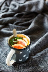 Hot tea with mint and grapefruit in gray vintage mug with stars on a gray rug. Winter xmas holidays concept.