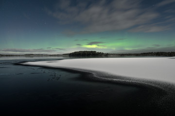 Aurora Borealis aka northern lights seen behind partly iced lake at winter night in Kurjenrahka National Park, Finland