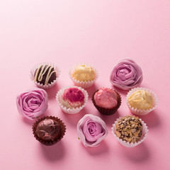 Assorted chocolates of dark and white chocolate on a pink background decorating flowers....