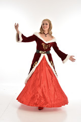 Fototapeta premium full length portrait of pretty blonde lady wearing red and white christmas inspired costume gown, standing pose on white background.