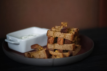 Rye crumbs in olive and garlic sauce on a red big plate on a black wooden background. Places for your text. Soft focus.