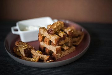 Rye crumbs in olive and garlic sauce on a red big plate on a black wooden background. Places for your text. Soft focus.