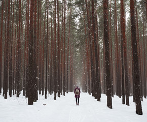 Lonely girl with a backpack walking along the fabulous forest. Large snowflakes and beautiful tree trunks.