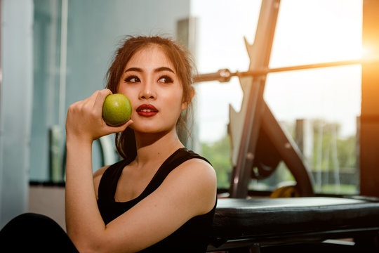 Asian woman exercising in the gym, Young woman workout in fitness for her healthy and office girl lifestyle. She is eating an apple.
