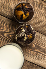 Two chocolate cupcakes and a glass of milk on a wooden table
