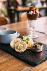 Grilled pork topped with cilantro and served with an English muffin, pickled vegetables and crumbed pistachios. served in black stone plate.
