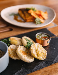 Grilled pork topped with cilantro and served with an English muffin, pickled vegetables and crumbed pistachios. served in black stone plate.