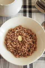 Boiled buckwheat with butter in white plate on checked table-cloth vertical